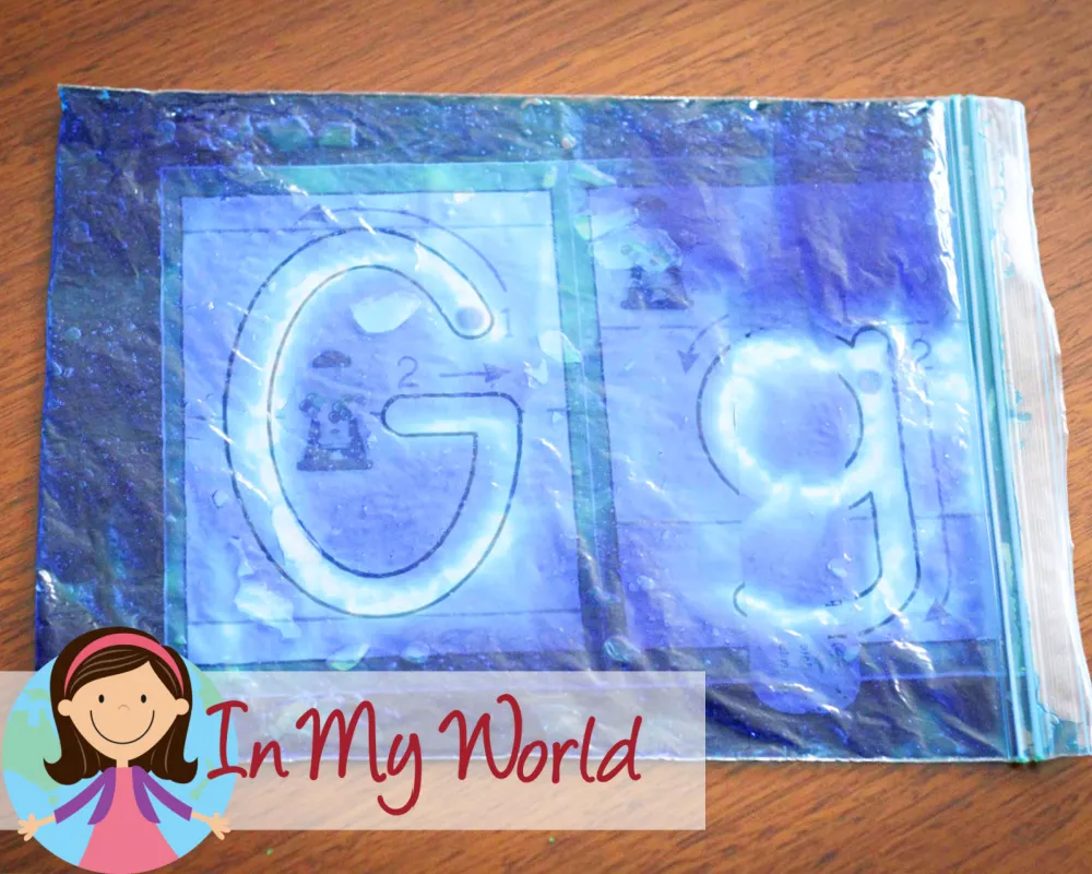 Child tracing the letter G on a gel bag placed over an alphabet poster to practice correct letter formation in a fun sensory way. Free downloads available on the blog.