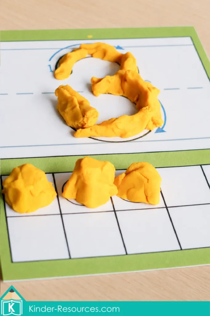 Yellow play dough forming numeral 3 with three matching pieces on a counting mat used during preschool letter K activities.