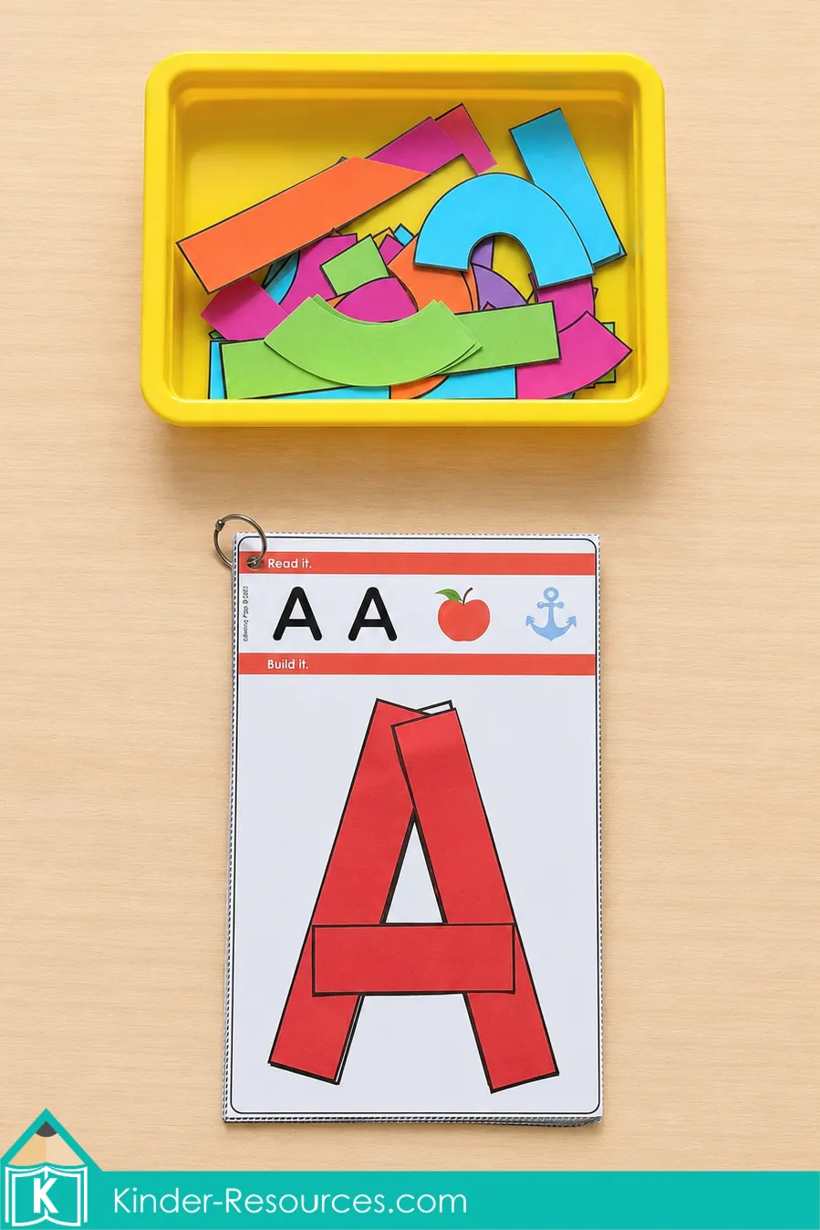 Building uppercase A with red printable pieces on a ring-bound alphabet card below a yellow tub.