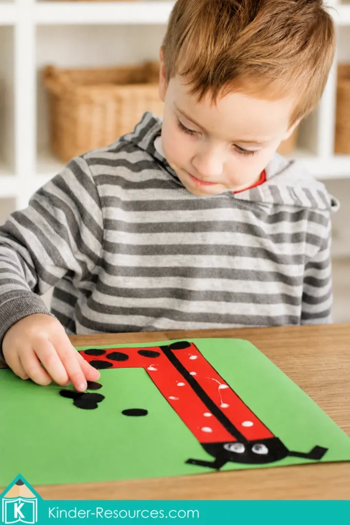 Child gluing black paper spots onto an uppercase letter L ladybug craft during a preschool alphabet art and fine motor activity.