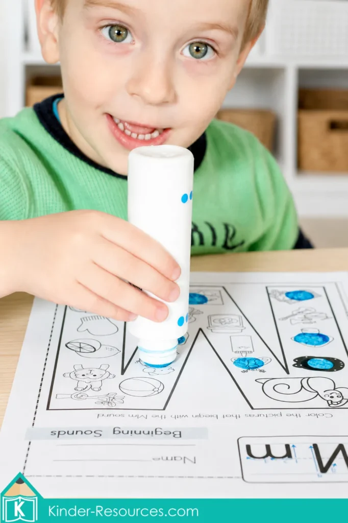 Child using a blue bingo dauber to identify pictures beginning with M on a preschool letter M beginning sounds worksheet.