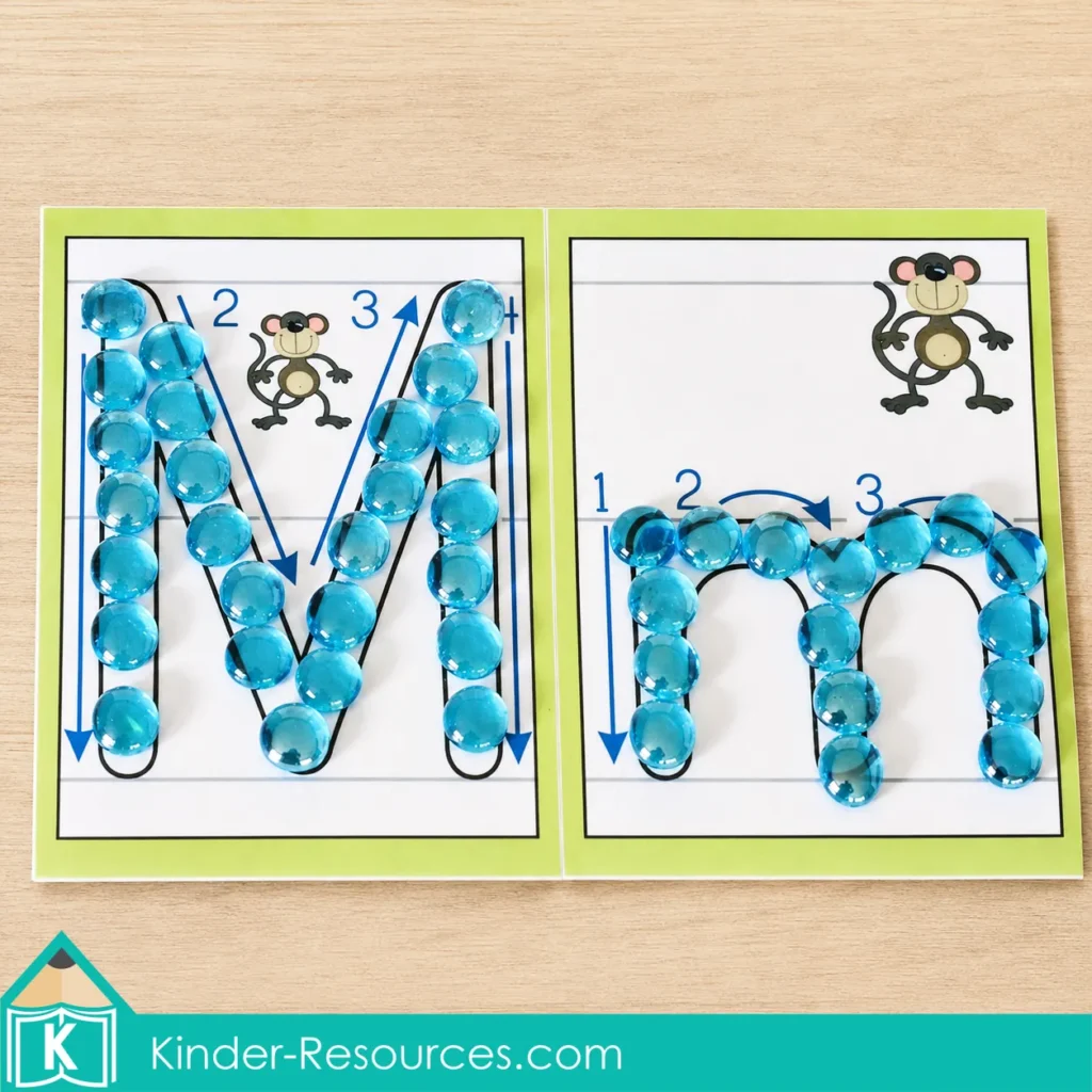 Translucent blue glass gems arranged along uppercase M and lowercase m formation paths for preschool alphabet and fine motor practice.
