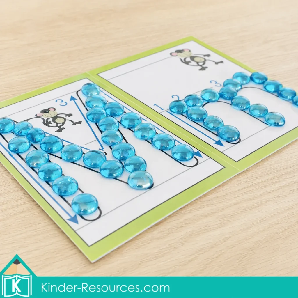 Translucent blue glass gems arranged along uppercase M and lowercase m formation paths for preschool alphabet and fine motor practice.