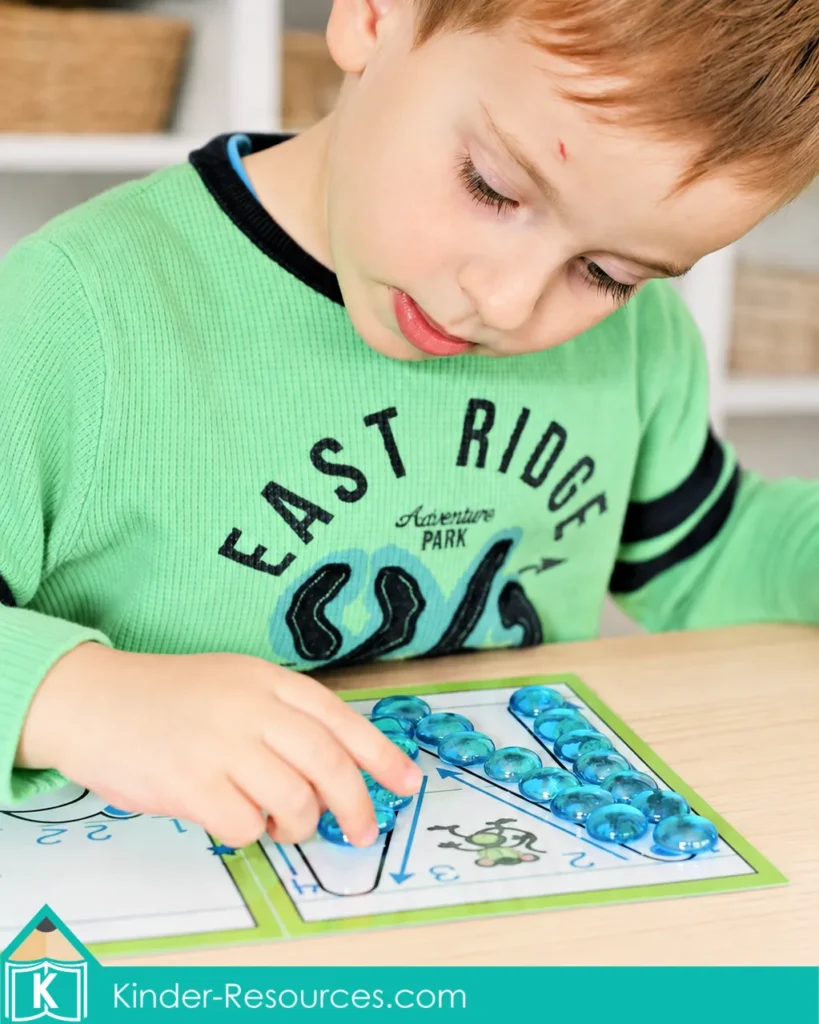 Child placing translucent blue glass gems along an uppercase m formation mat for preschool Letter M recognition and fine motor practice
