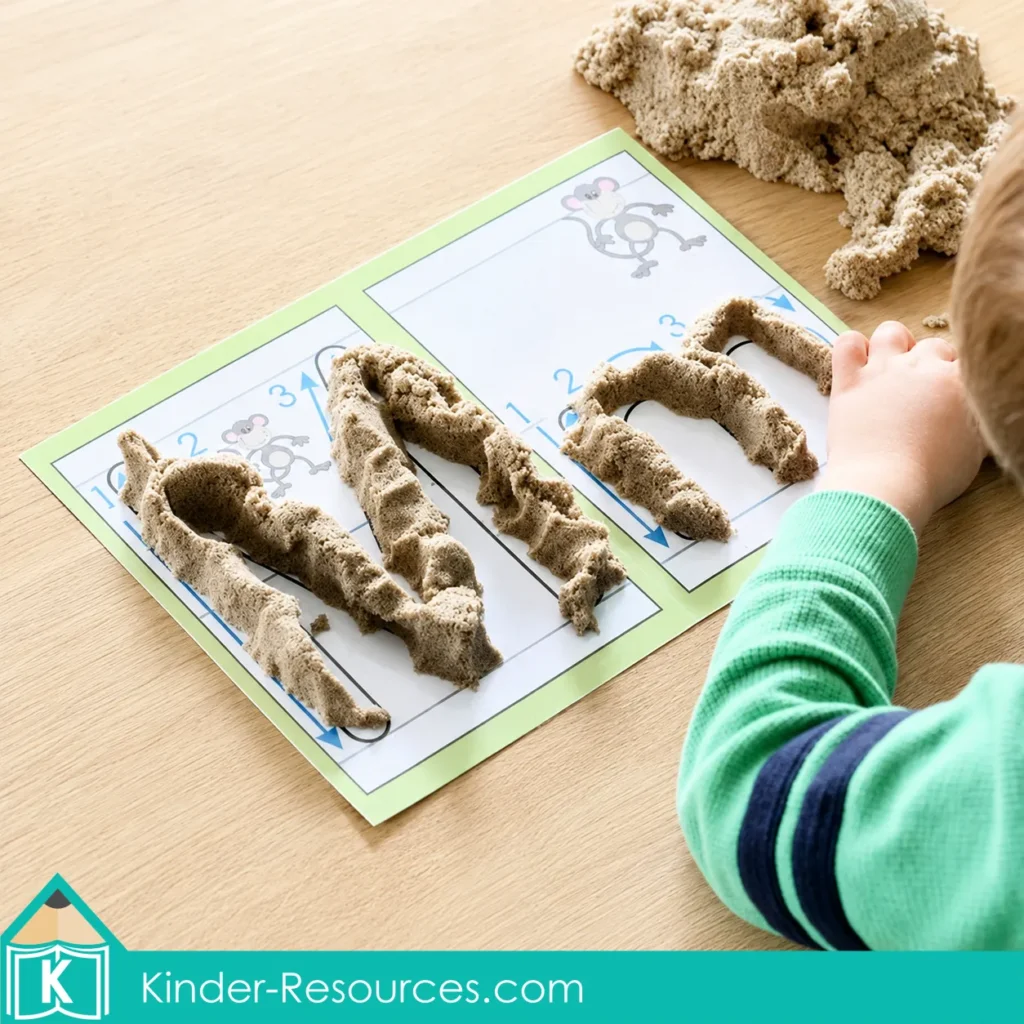 Child forming uppercase M and lowercase m with crumbly sensory sand on preschool alphabet mats for tactile letter and fine motor practice.