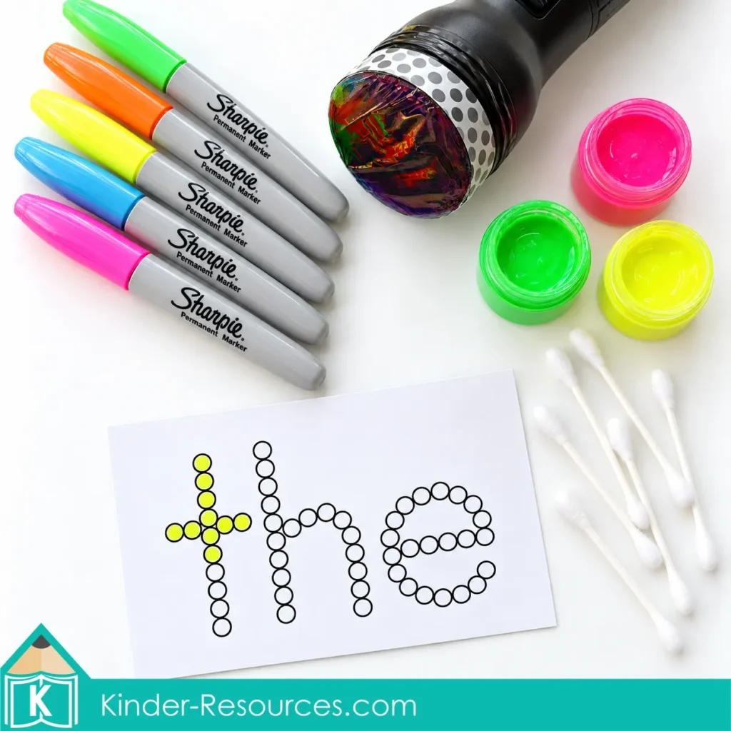Neon markers, fluorescent paint, cotton swabs, flashlight, and sight word card on a white background
