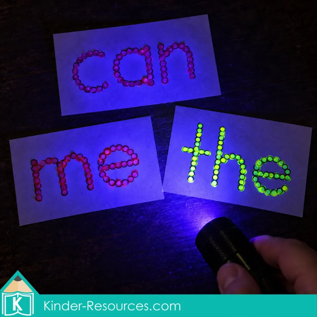 Hand shining a blacklight flashlight over the sight words can, me, and the
